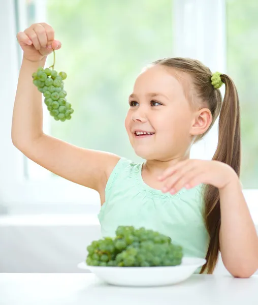 Cute little girl is looking at green grapes — Stock Photo, Image