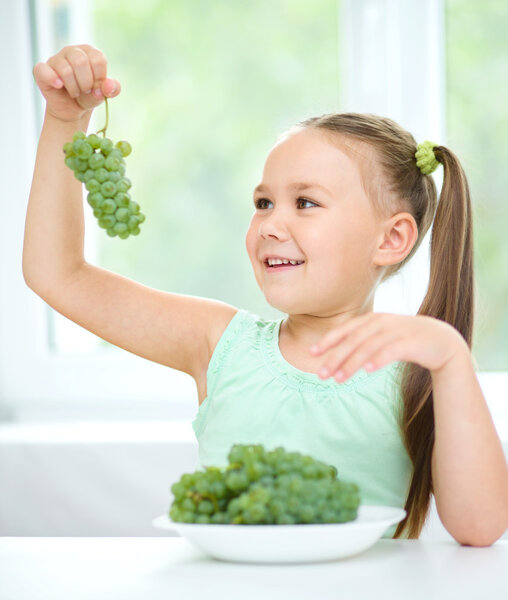 Cute little girl is looking at green grapes