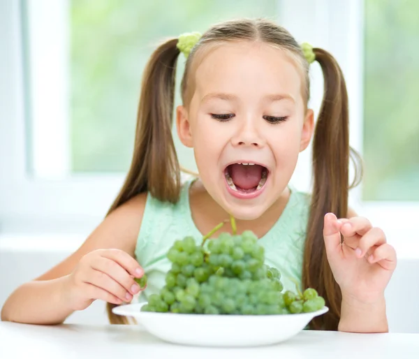 Cute little girl is eating green grapes — Stock Photo, Image