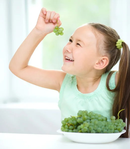 Cute little girl is looking at green grapes — Stock Photo, Image