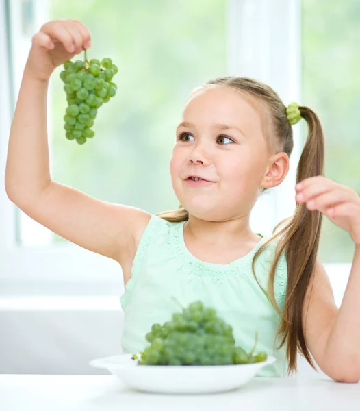 Cute little girl is looking at green grapes — Stock Photo, Image