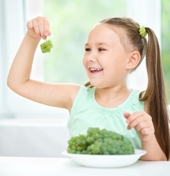 Cute little girl is looking at green grapes