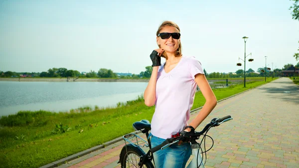 Mujer joven está de pie detrás de la bicicleta — Foto de Stock