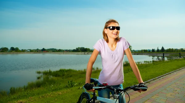 Mujer joven está de pie detrás de la bicicleta — Foto de Stock