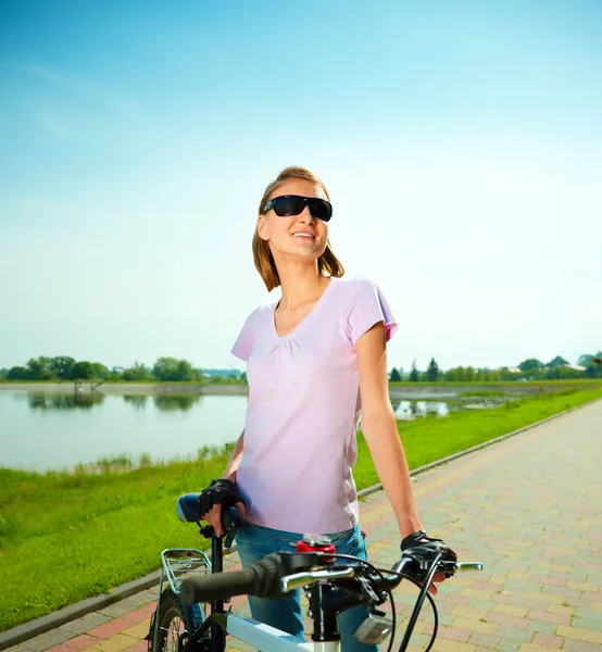 Jovem mulher está atrás da bicicleta — Fotografia de Stock