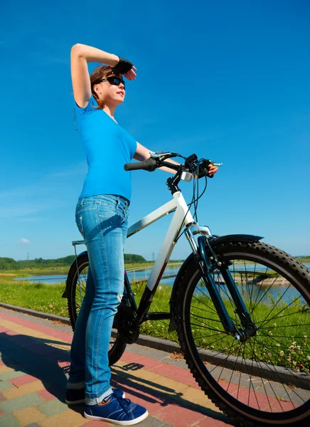 Jovem mulher está de pé na frente de sua bicicleta — Fotografia de Stock