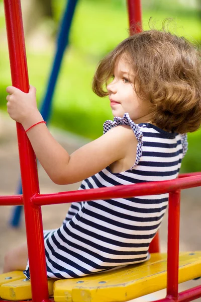 Giovane ragazza felice sta oscillando nel parco giochi — Foto Stock