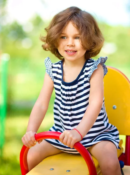 Jovem menina feliz está balançando no playground — Fotografia de Stock