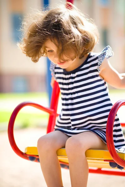 Jovem menina feliz está balançando no playground — Fotografia de Stock