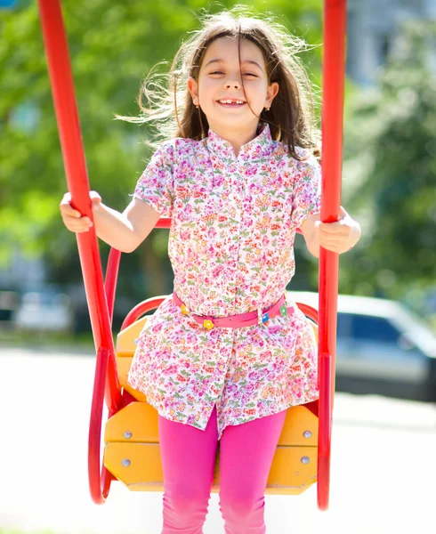 Jovem menina feliz está balançando no playground — Fotografia de Stock