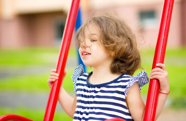 Jovem menina feliz está balançando no playground — Fotografia de Stock