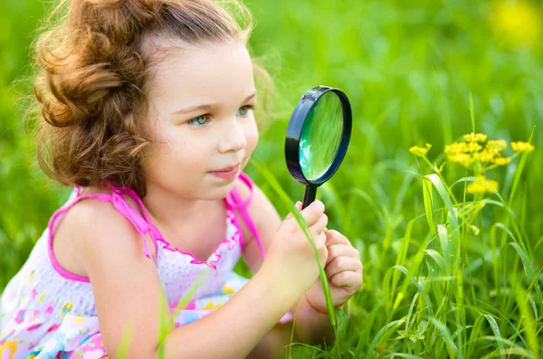 Ung flicka är ute på flower genom förstoringsglas — Stockfoto