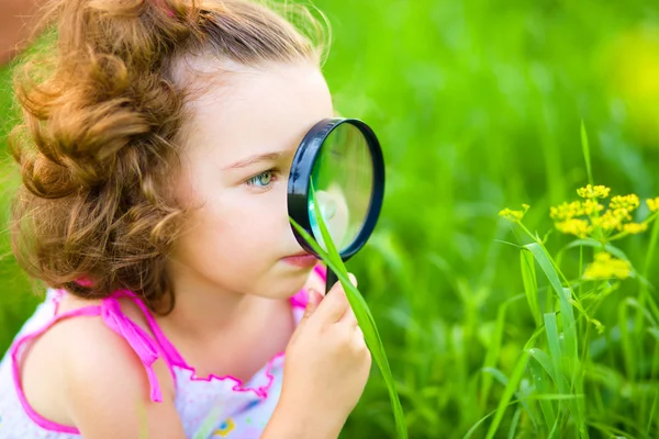 Young girl is looking at flower through magnifier — Stock Photo, Image