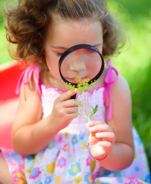 Young girl is looking at flower through magnifier — Stock Photo, Image