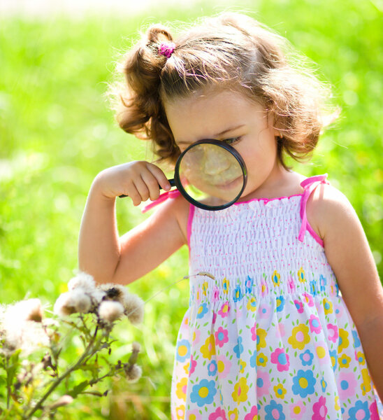 Young girl is looking at flower through magnifier