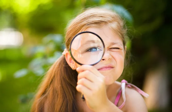 Liten flicka tittar genom förstoringsglas — Stockfoto