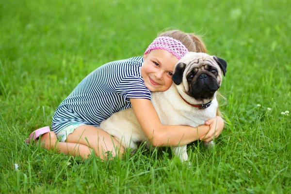 Little girl and her pug dog on green grass — Stock Photo, Image