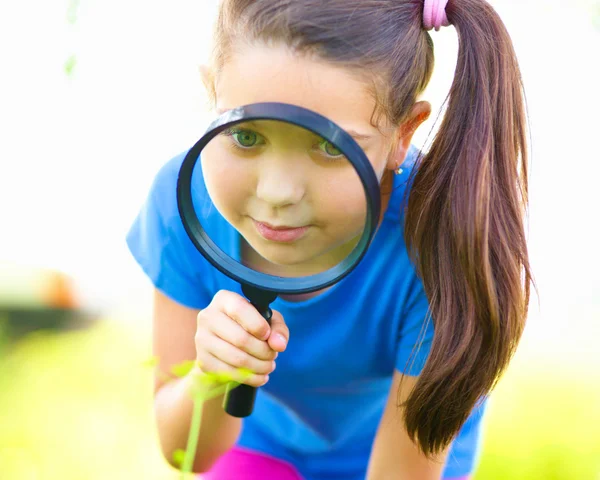 小さな女の子は拡大鏡を通して見る — ストック写真