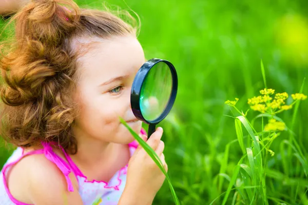 Молода дівчина дивиться на квітку через збільшувач — стокове фото