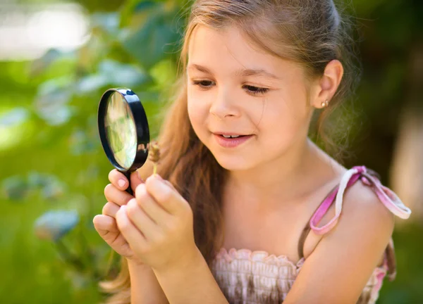 Young girl is looking at flower through magnifier — Stock Photo, Image