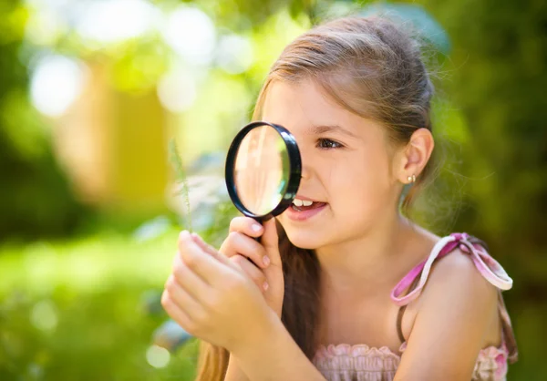 Young girl is looking at flower through magnifier — Stock Photo, Image