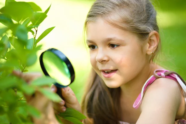 Meisje kijkt boom bladeren door vergrootglas — Stockfoto