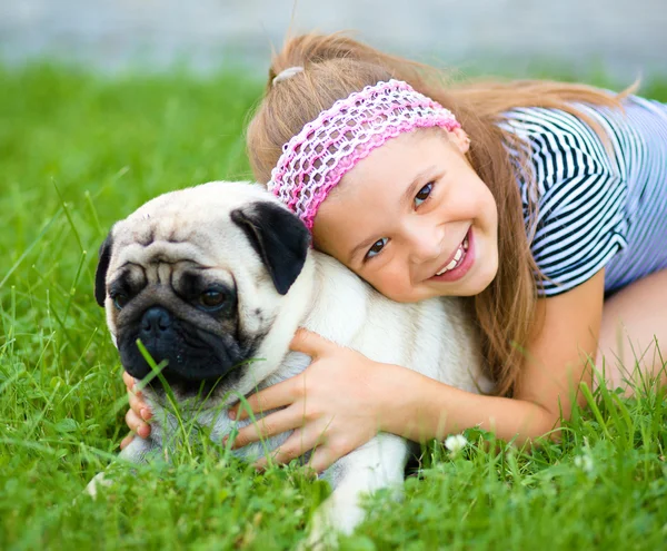 Маленькая девочка и ее мопс на зеленой траве — стоковое фото