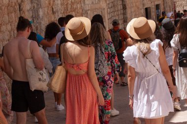 Two young girls in summer clothes seen from behind stroll with other tourists in an ancient southern European district. Dubrovnik, Croatia - July 13, 2022.