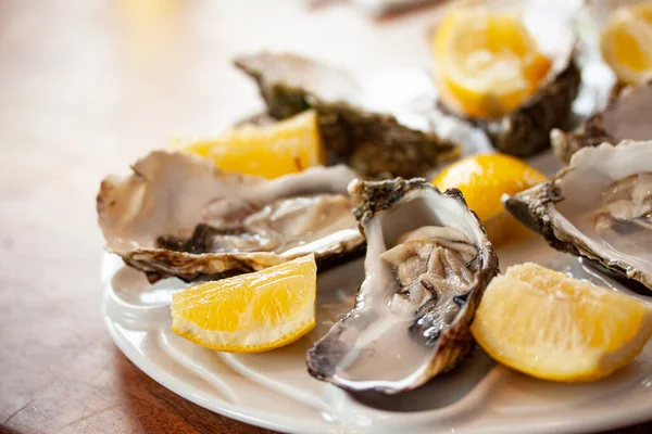 Fresh oysters close-up on a white plate, served table with lemon. Healthy sea food. Dinner of fresh oysters in a restaurant. Selective focus with shallow depth of field.