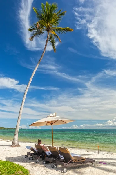 Tjejen sitter på strandstolar under palm löv på den sh — Stockfoto
