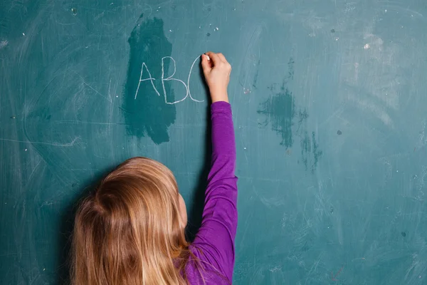 Jong meisje schrijven van brieven op schoolbord — Stockfoto