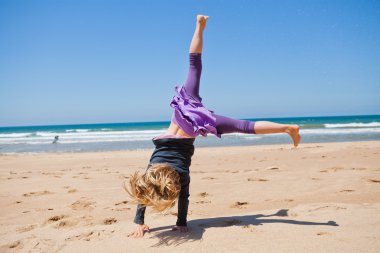 Young girl doing cartwheel at beach clipart