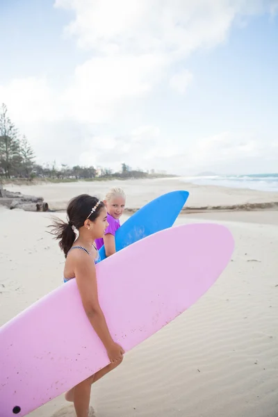 Twee leuke jonge meisjes lopen samen met surfplanken op strand — Stockfoto