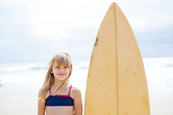 Smiling young girl standing next to surfboard — Stock Photo, Image