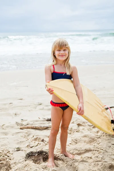 Smiling young girl holding surfboard on beach — Stock Photo, Image