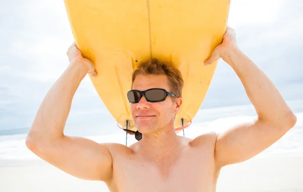 Lächelnder Mann legt Surfbrett auf den Kopf am Strand — Stockfoto