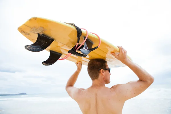 Człowiek spoczywała deska surfingowa na głowę na plaży — Zdjęcie stockowe