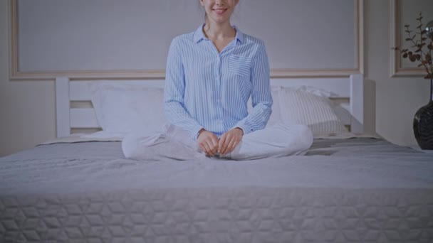 Blonde female wearing pajamas sits in bedroom — ストック動画