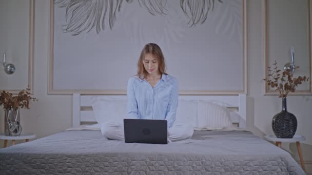Blonde female wearing pajamas works in bedroom — ストック動画