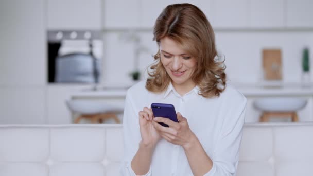 Mensajes de texto femeninos alegres en el móvil en apartamento — Vídeo de stock