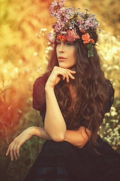 Young beautiful woman portrait with wreath of flowers in field summer day retro colors