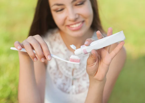 Ung kvinna håller en tandborste och utsläppande tandkräm på det. — Stockfoto