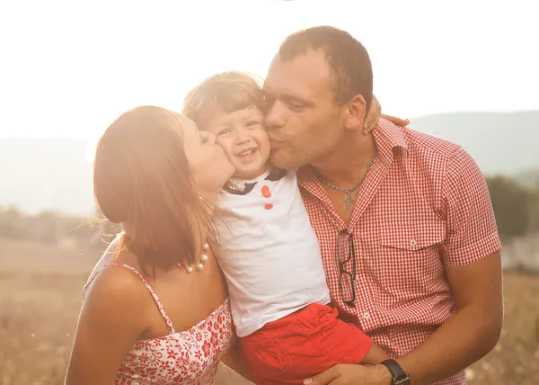 Happy mother and father kissing their daughter in the park — Stock Photo, Image