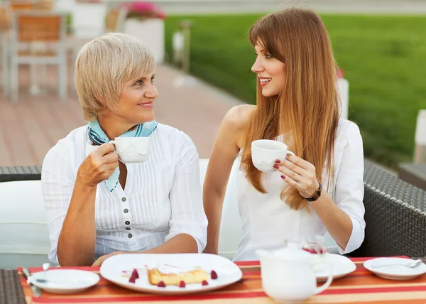 Adult mother and daughter drinking tea or coffee. They communicate sitting outside in a cafe. — Stock Photo, Image