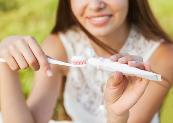 Молодая женщина держит зубную щётку и кладёт на неё зубную пасту. . — стоковое фото
