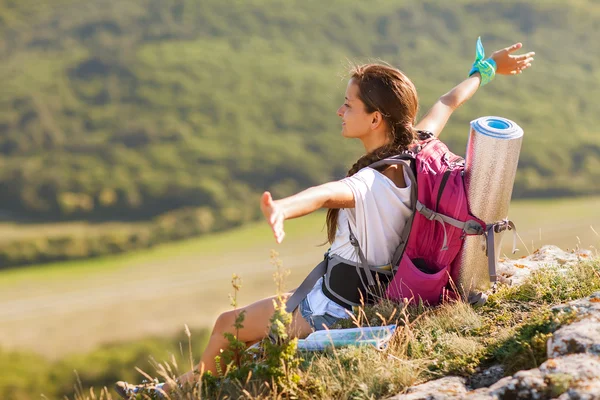 Young woman with backpack sitting on cliff's edge and looking to — Stock Photo, Image