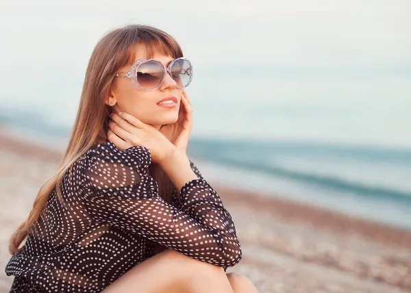 Fashion girl sitting on the beach wearing sunglasses — Stock Photo, Image