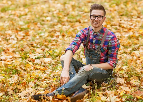 Hipster chico sentado en el otoño parque sonriendo — Foto de Stock