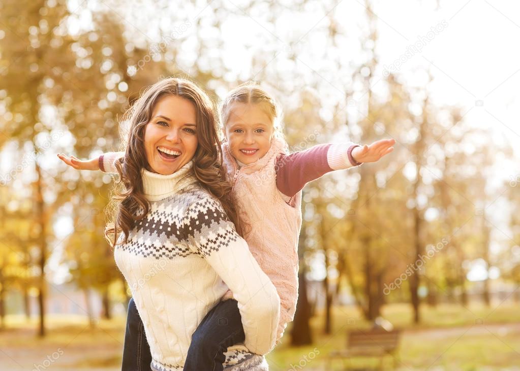 Mother giving daughter piggyback ride in autumn woodland