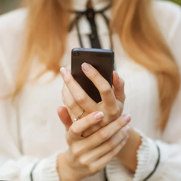 Jonge mooie vrouw schrijft een sms naar uw mobiele telefoon. — Stockfoto